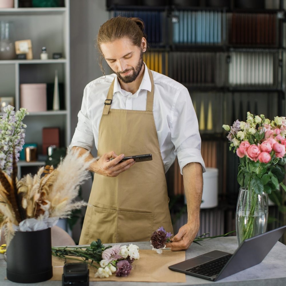 Florists making bouquet of flowers on counter and taking photo on smartphone for social media.